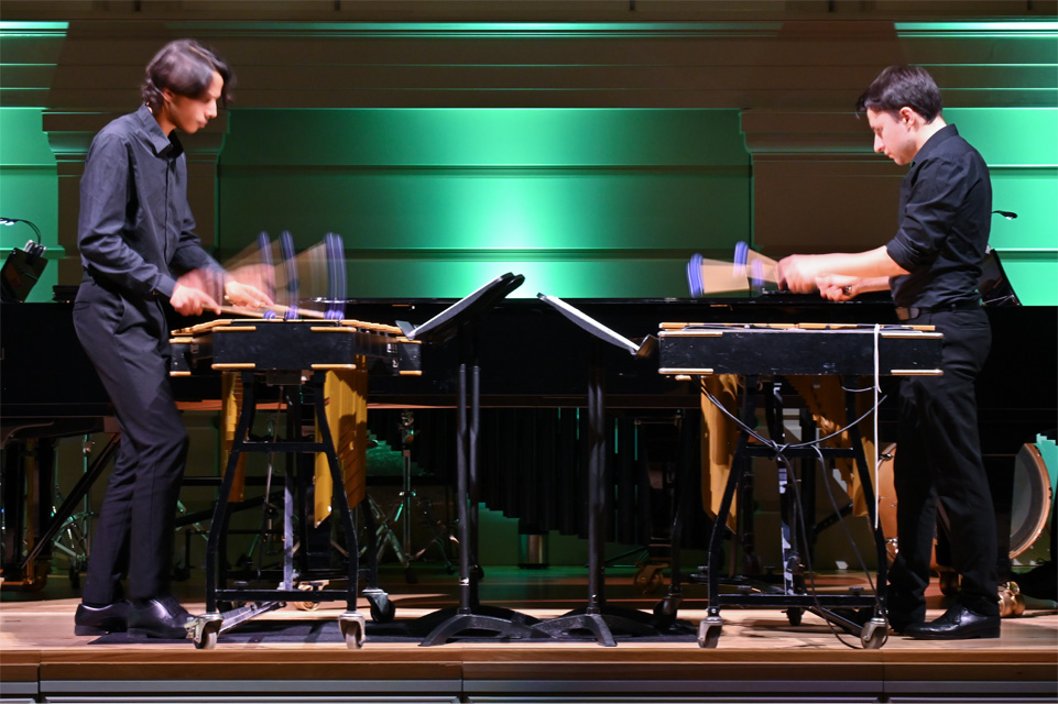 Students, wearing formal attire, performing two marimbas across from each other, on a stage.